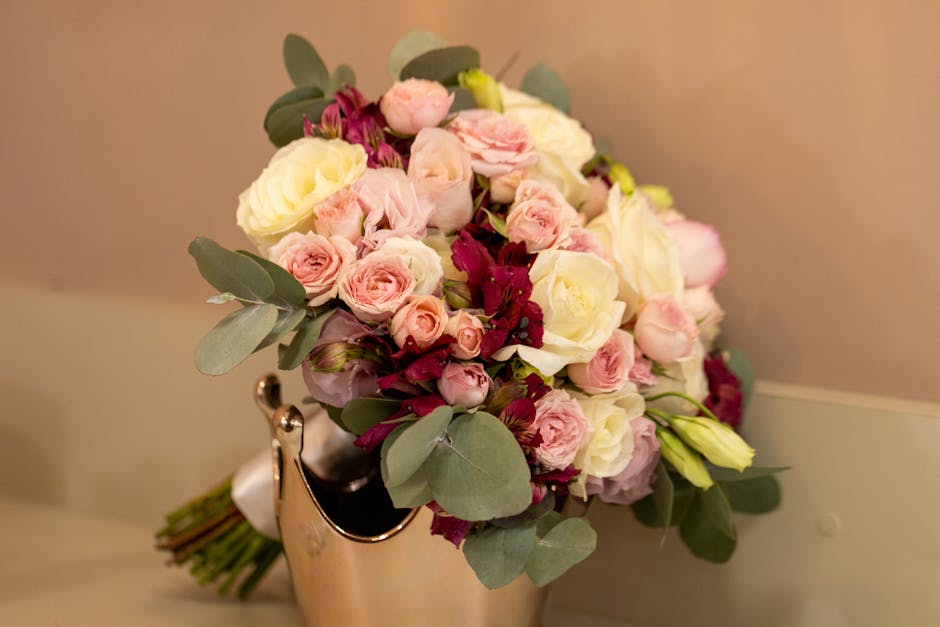A floral arrangement featuring a bouquet of fresh flowers, including pale pink roses, white roses, deep burgundy blooms, and light green buds, complemented by eucalyptus leaves with round, muted green