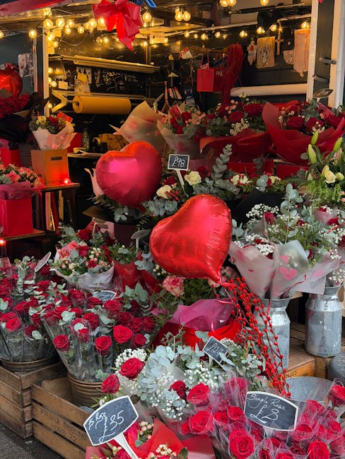 A vibrant display of floral gifts at a flower shop, featuring a variety of red and white roses, mixed with greenery and white accents. Arranged in baskets, wrapping papers, and bouquets, some with red